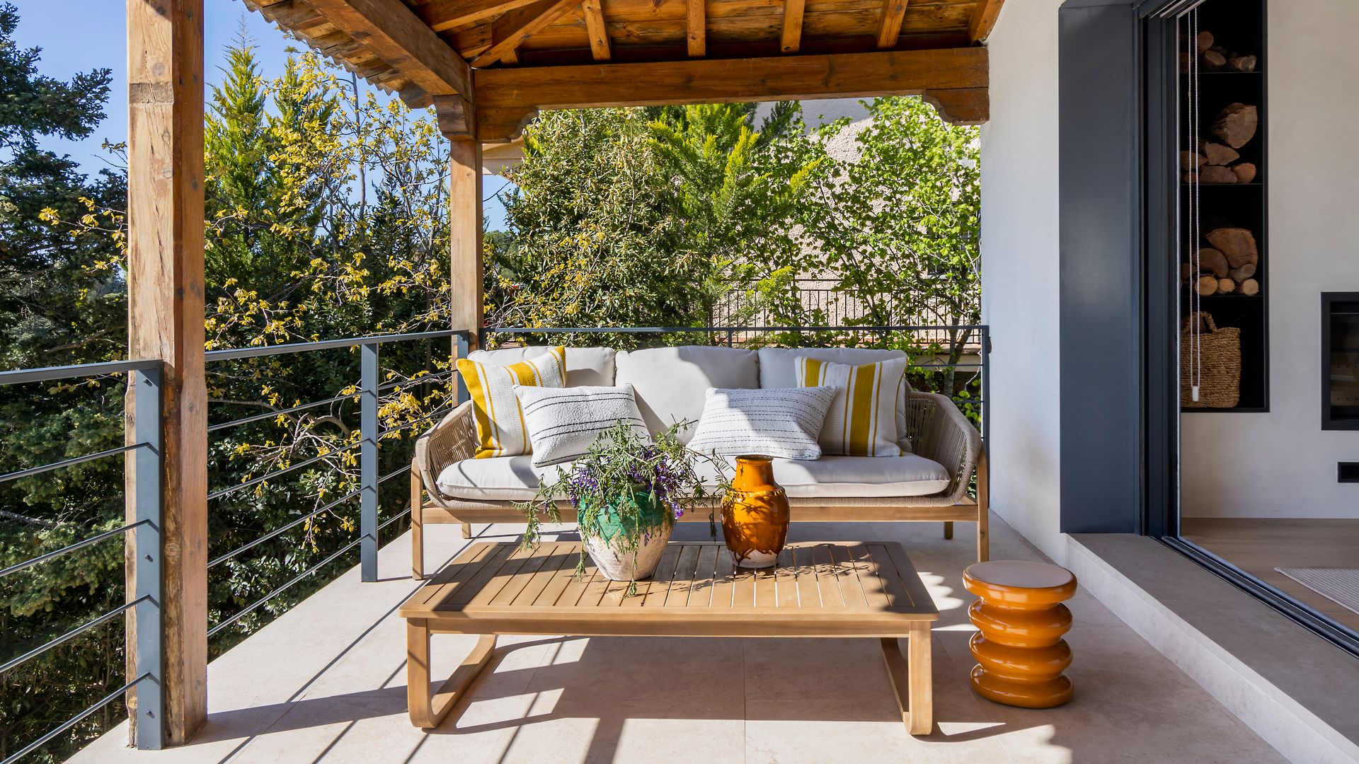 Terraza con porche cubierto de madera, salón exterior, barandilla negra y muebles de madera 
