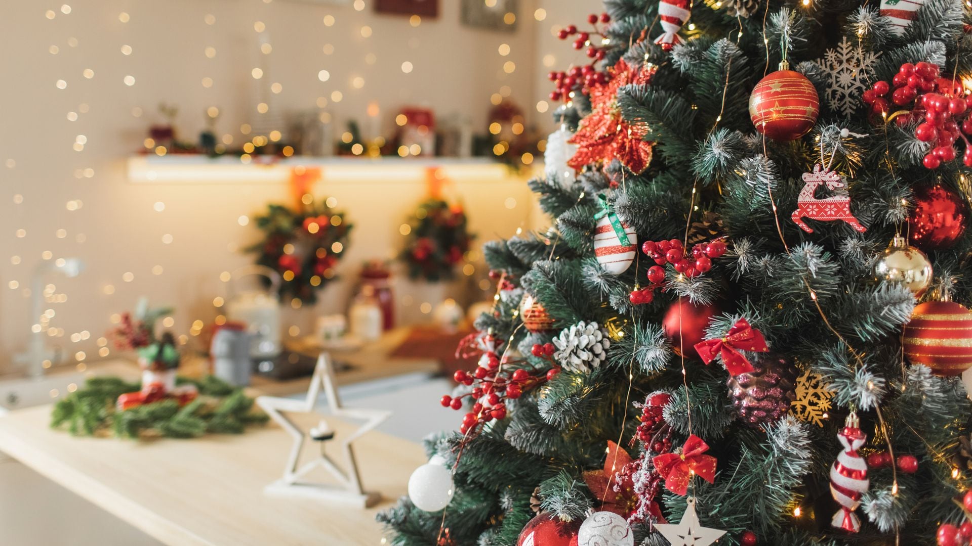 Cocina en blanco y madera decorada por Navidad con un árbol en blanco, rojo y verde, con detalles sobre la encimera.