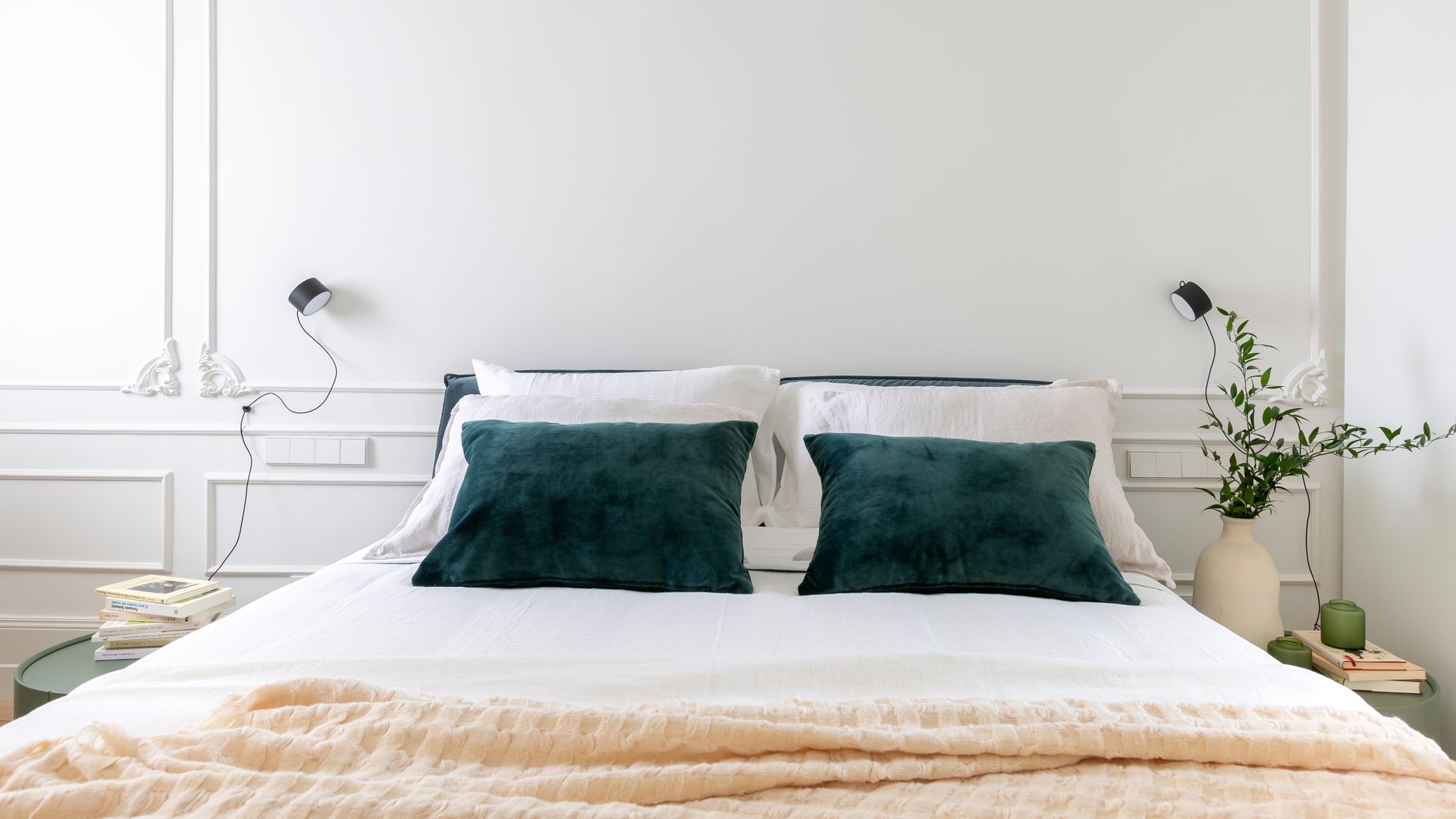 Dormitorio con pared del cabecero con molduras blancas, ropa de cama blanca, cojines verdes, jarrón con plantas verdes, mesita de noche verde, apliques de pared 