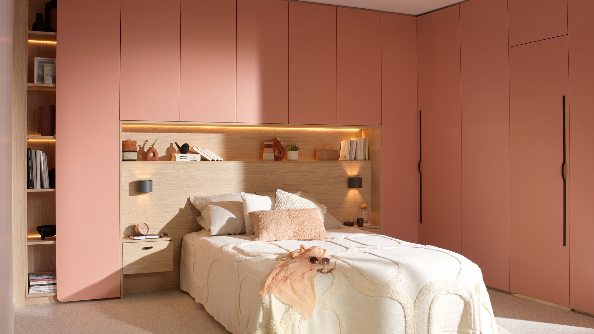 Dormitorio con estructura a medida rosa salmón con cabecero integrado de madera, estantería, armario ropero y módulos de armario, ropa blanca de cama, alfombra 