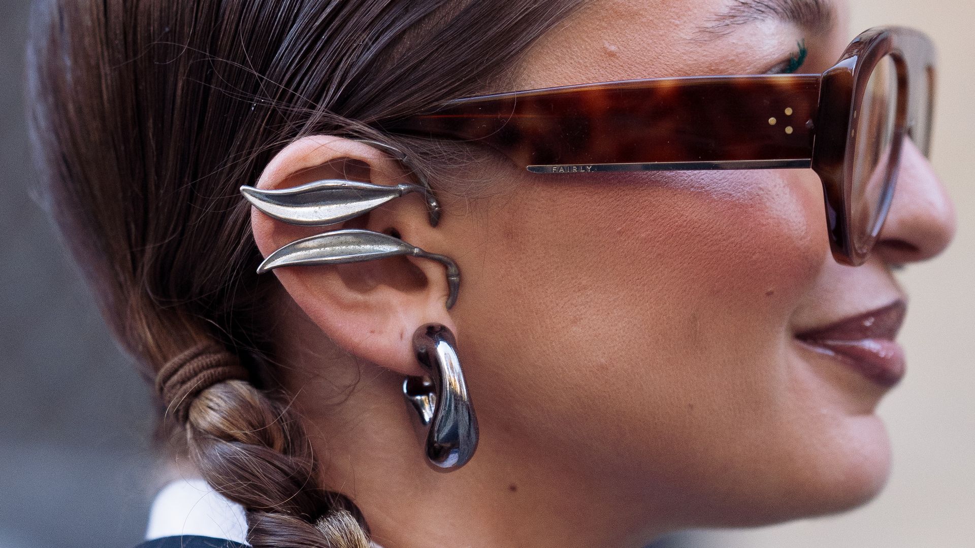 Chica joven de perfil con trenzas en el pelo, gafas de sol y grandes joyas de plata.