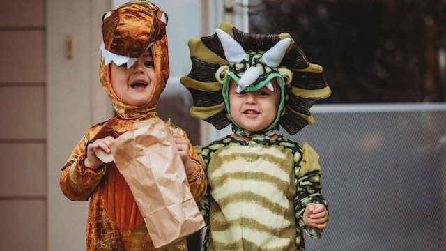 Niños disfrazados de dinosuarios, uno naranja y uno verde, en el jardín de casa o en la calle, sonriendo para Carnaval