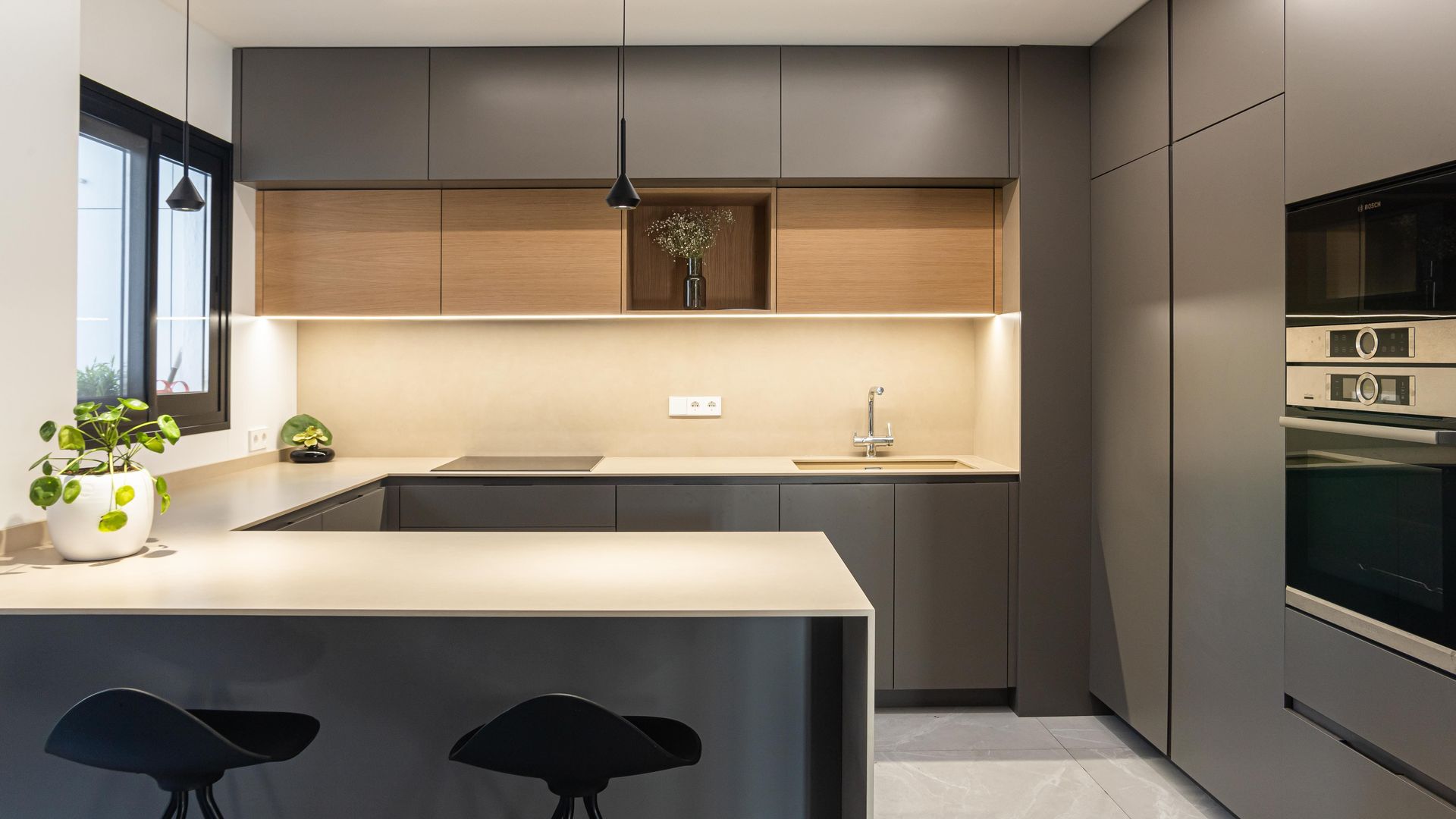 Cocina con península, muebles en color gris, luz perimetral en el techo, luz bajo los armarios superiores, encimera blanca