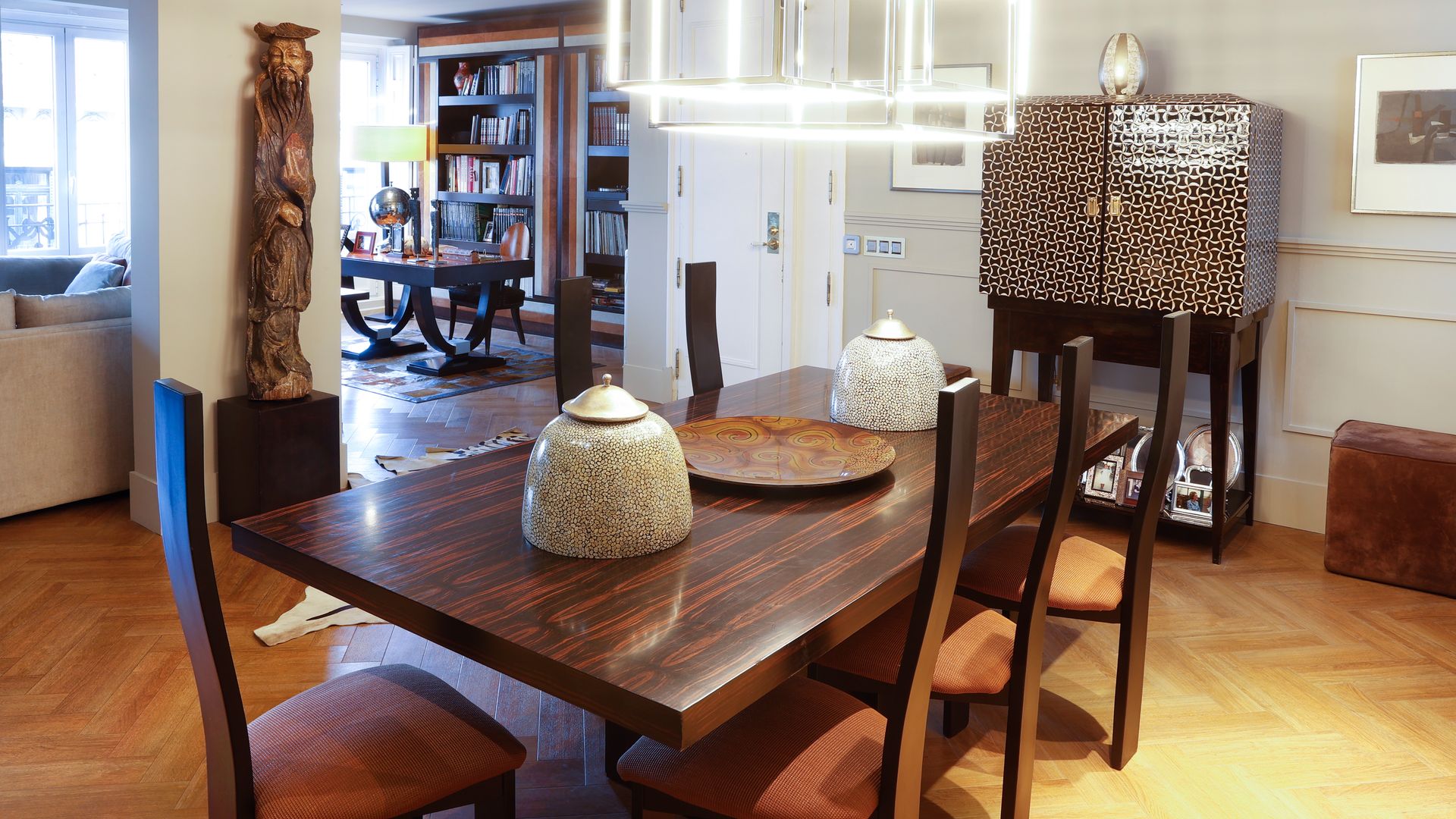 Comedor con mesa de madera oscura, sillas de madera con asiento tapizado, suelo de madera, lámpara de techo, mueble de estilo chino con cáscara de huevo, escultura con pedestal