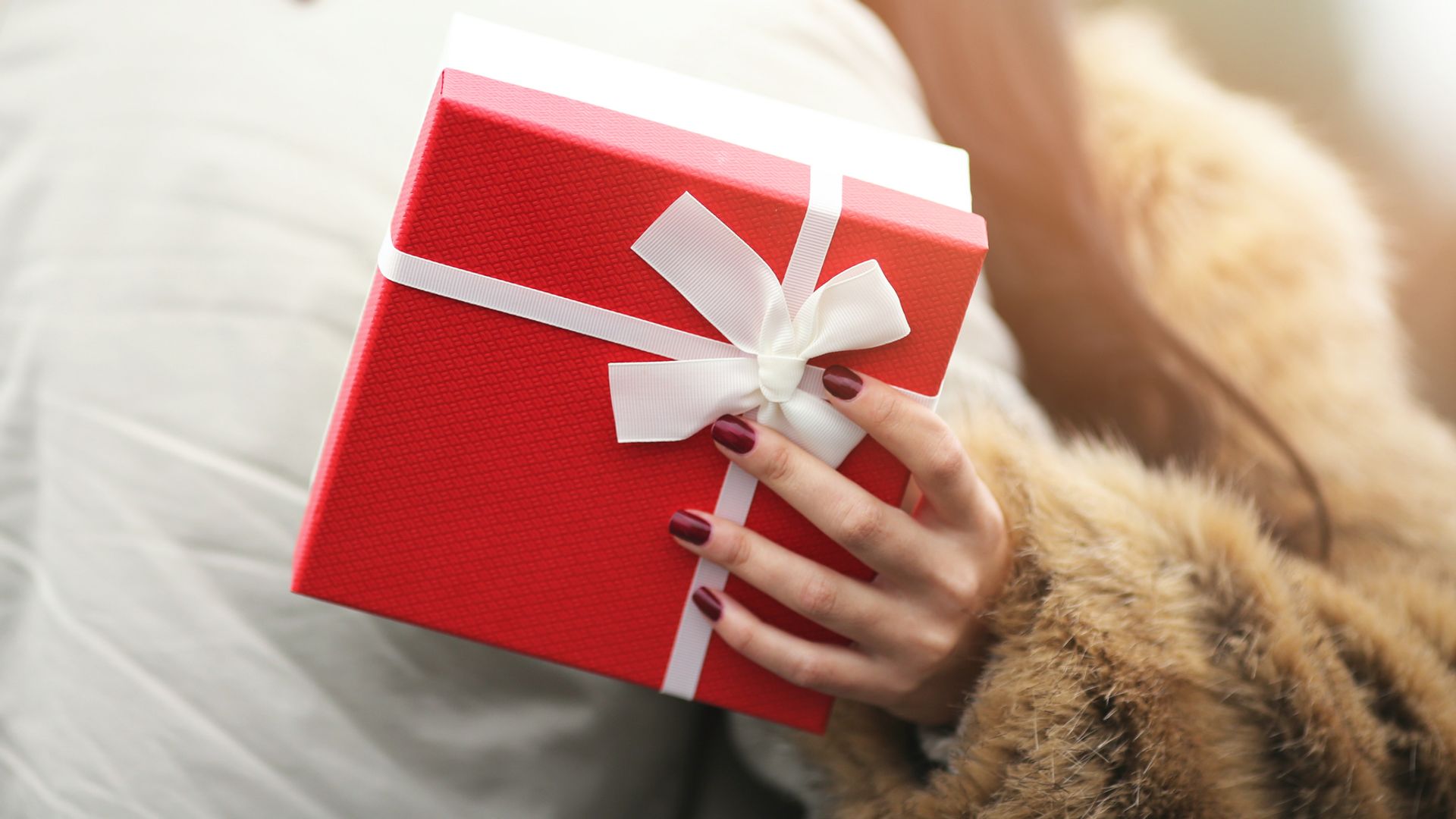 Mujer abrazando a un hombre con caja de regalo roja en la mano