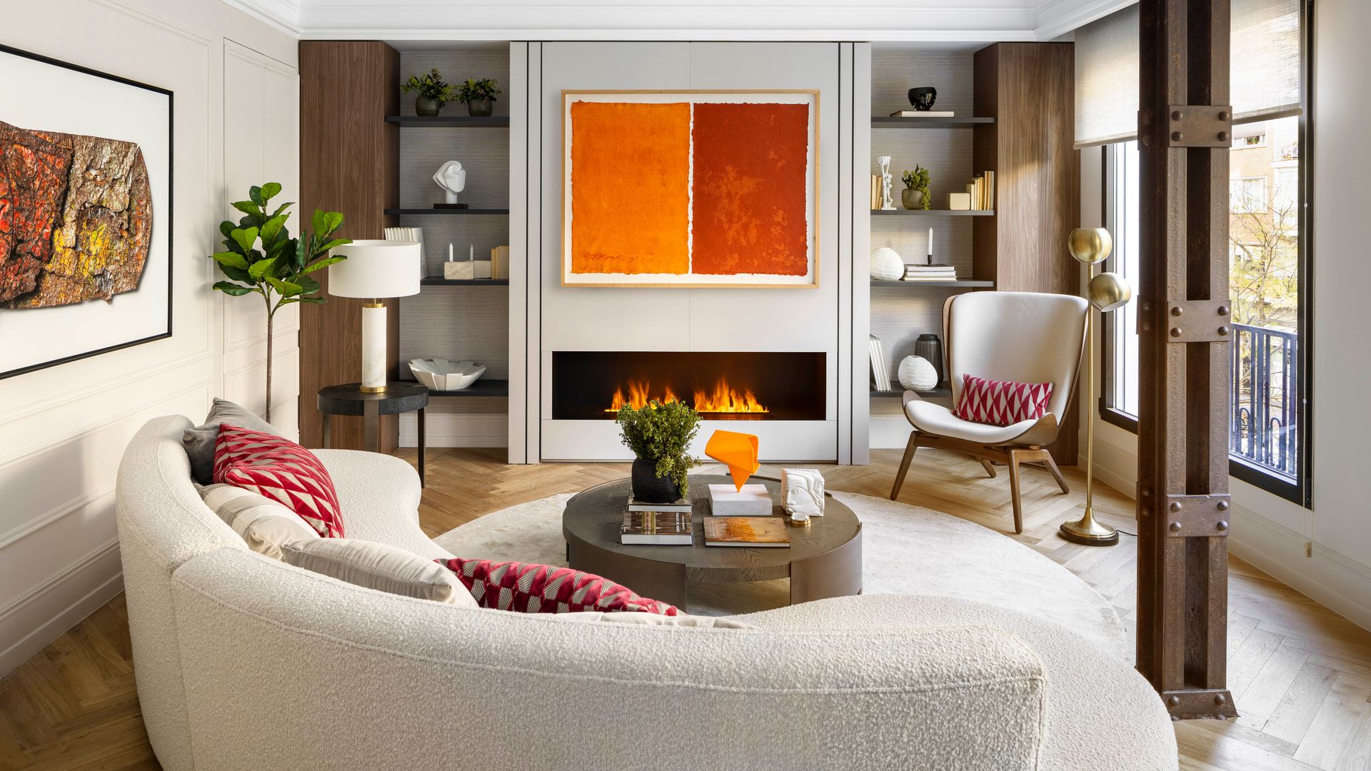 Salón con chimenea con sofá de formas curvas, blanco, vigas metálicas, chimenea moderna, cuadro de colores en la pared de la chimenea, butaca, blanca, lámpara de pie, librerías a medida a ambos lados de la chimenea