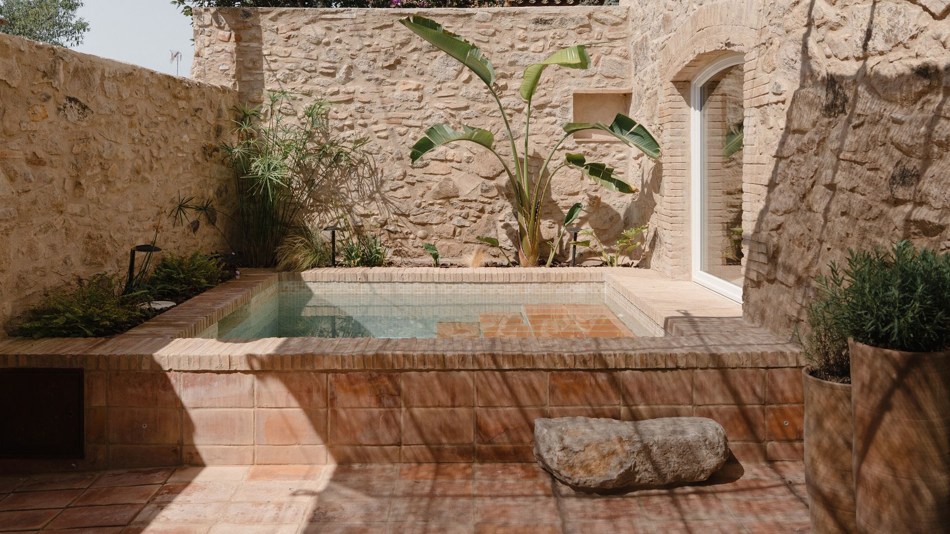 Piscina tipo alberca en un patio, con gres y paredes de piedra 