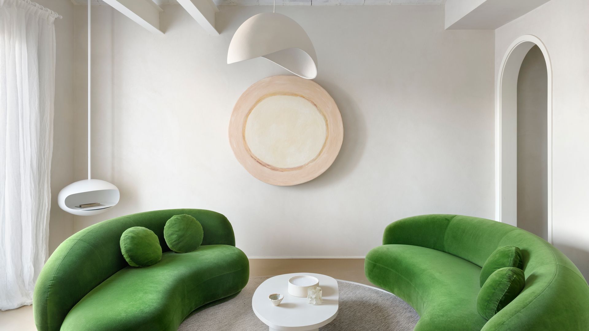 Salón con bóvedas catalanas pintadas de blanco, chimenea colgante, lámpara de techo, sofás curvos de color verde