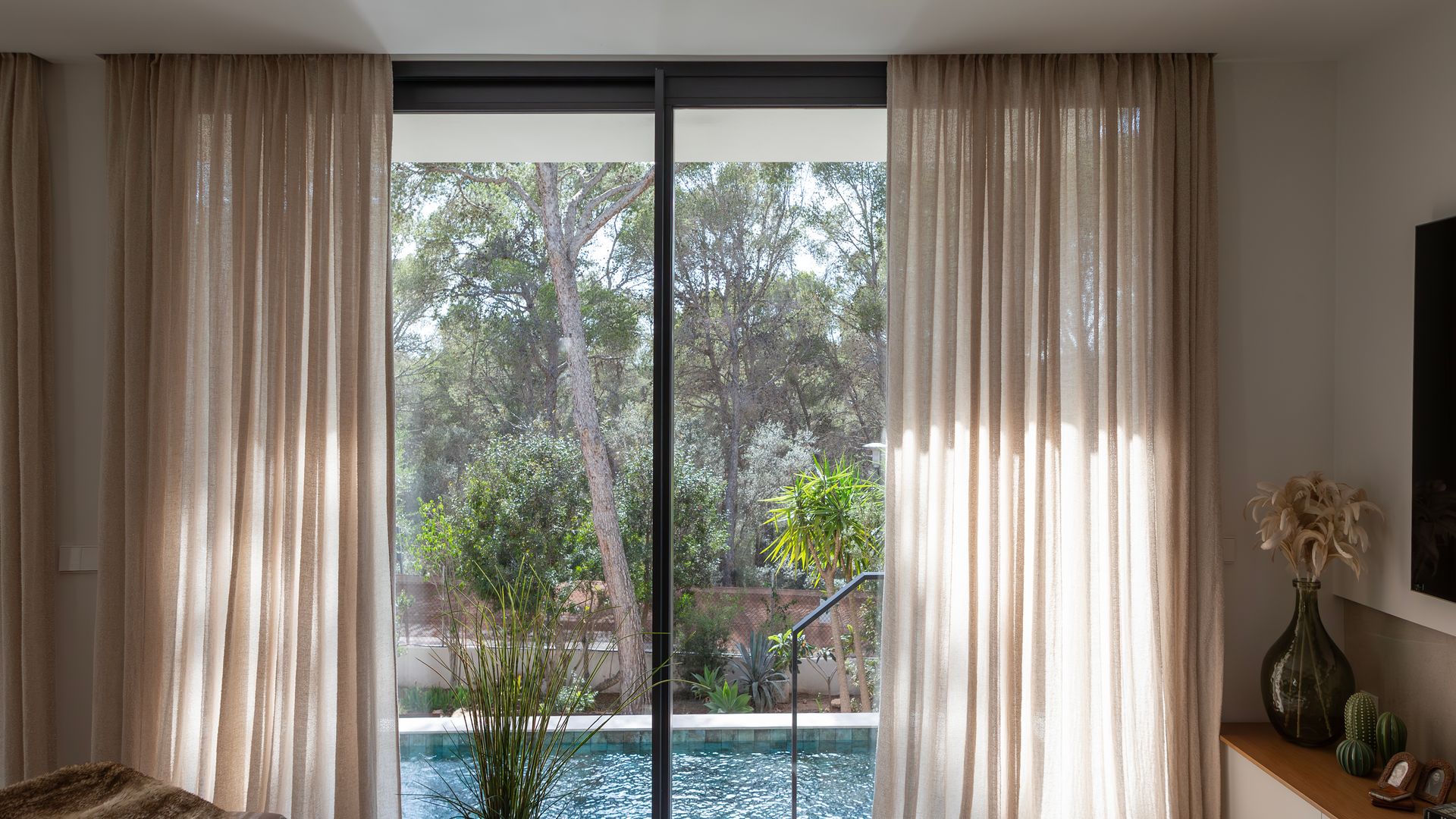 Salón con ventanal con vistas a la piscina, cortinas beiges hasta el techo