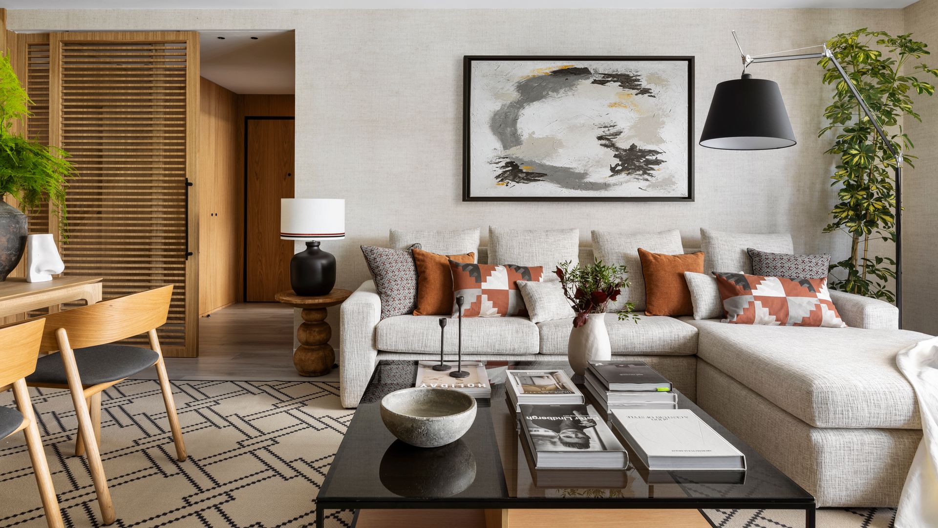 Salón comedor con puerta corredera de madera, sofá con chaise longue, alfombra, mesa de centro negra, lámpara de pie, cuadro en la pared, cojines marrones