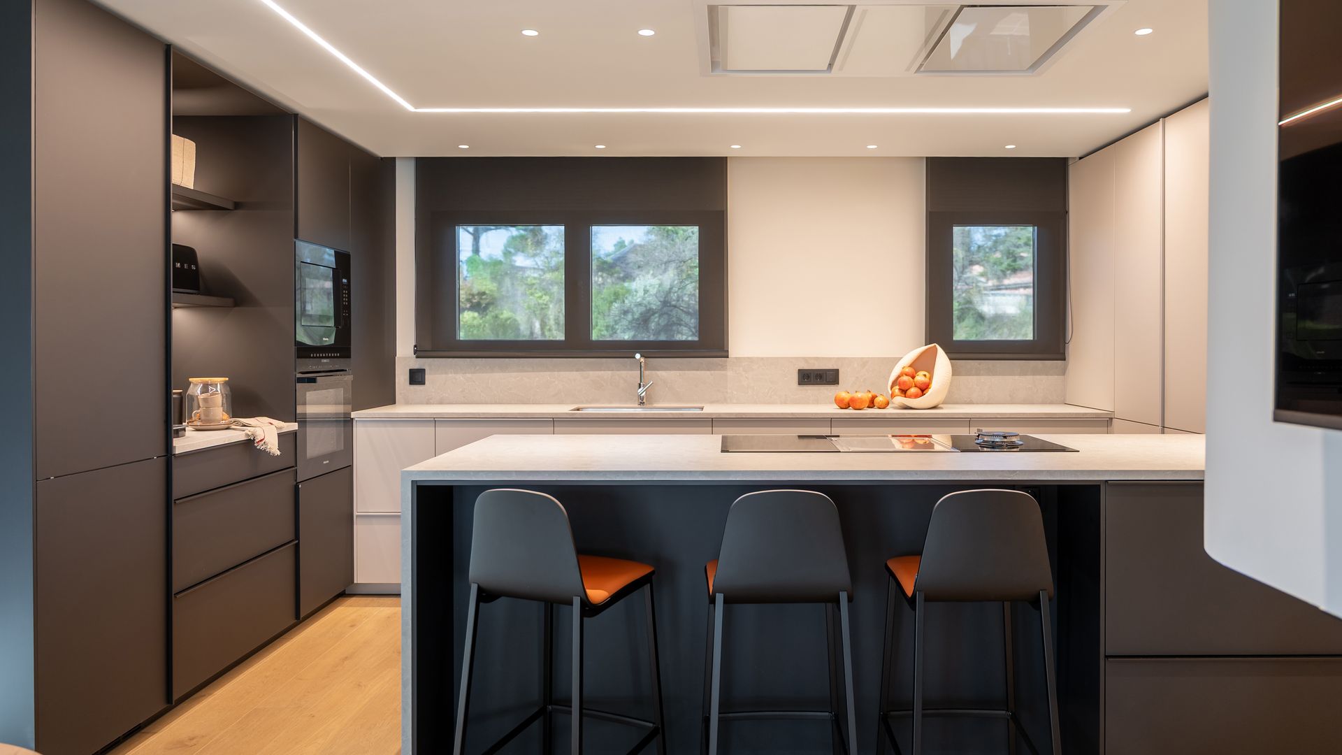Cocina con península con muebles argos y encimera blanca, luz en el techo, focos y bajo los armarios altos, campana de techo