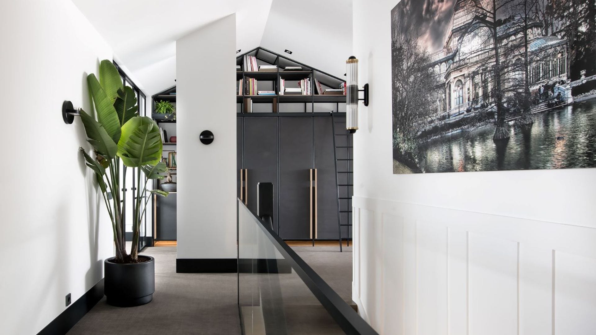 Buhardilla con librería negra hasta el techo en forma de tejado, escalera, planta en maceta negra, subida de escalera 