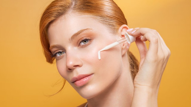 Rostro de mujer pelirroja con piel luminosa aplicándose sérum facial en la mejilla