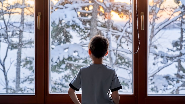 Niño delante de una ventana en invierno, dentro de casa