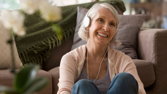 mujer madura sentada junto al sofá, escuchando música con unos auriculares