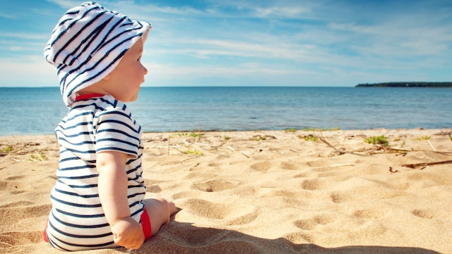 Bebé con gorro y camiseta sentado en la arena de la playa