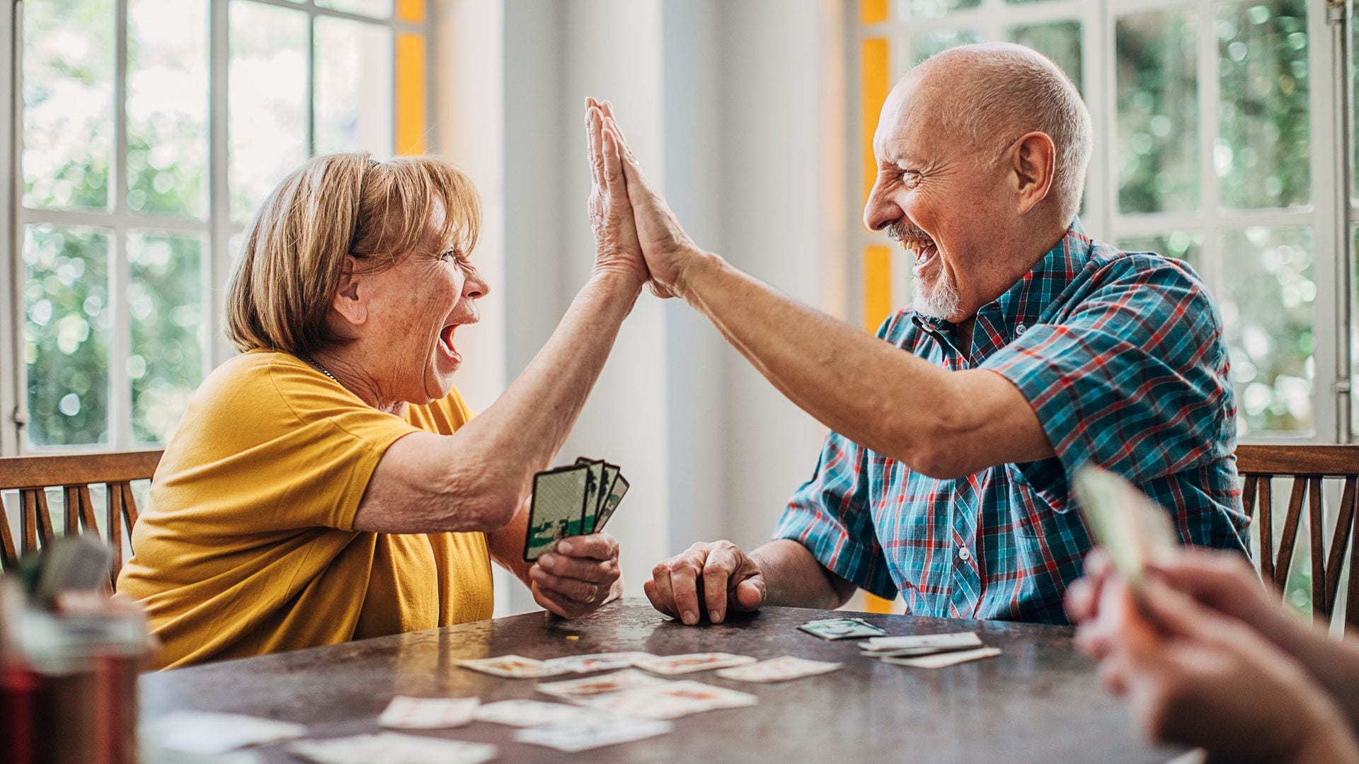 Dos personas mayores chocando la mano mientras están jugando a las cartas en una mesa.