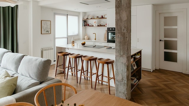 Salón, cocina y comedor, con columna vista de hormigón, suelo de madera, cocina blanca con taburetes de madera