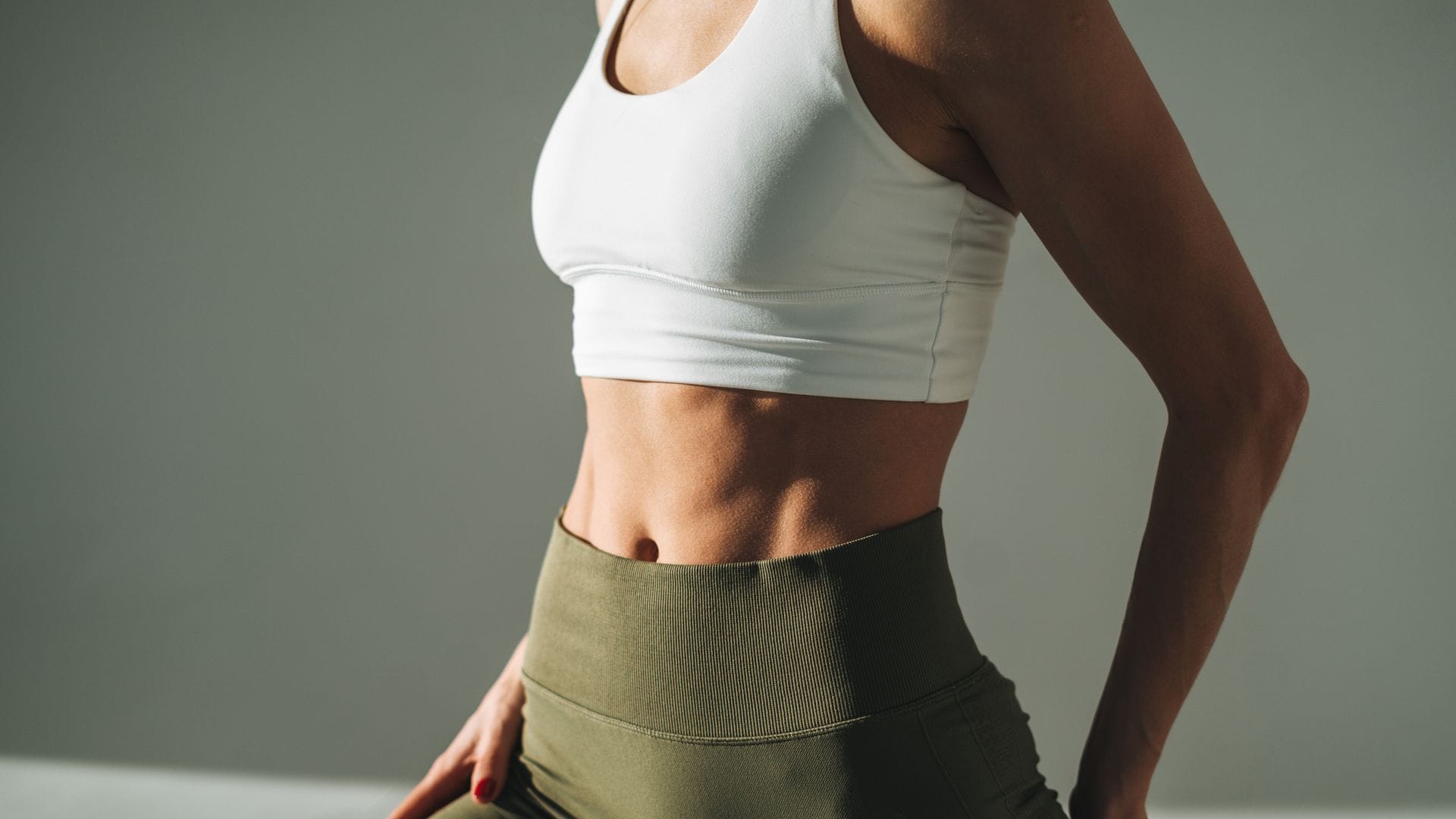 Mujer con abdomen tonificado y ropa deportiva con un plano detalle de su abdomen.