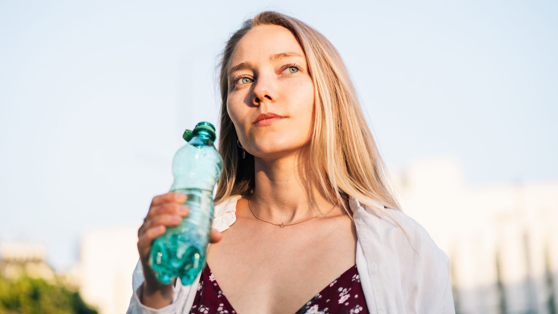 Mujer joven rubia de ojos azules con vestido de flores bebiendo agua en la calle