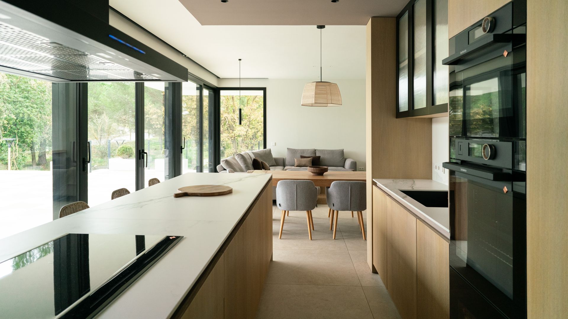 Cocina abierta al salón y al comedor con muebles de madera, vitrina con el marco negro, electrodomésticos en columna, isla de cocina en el centro con la placa