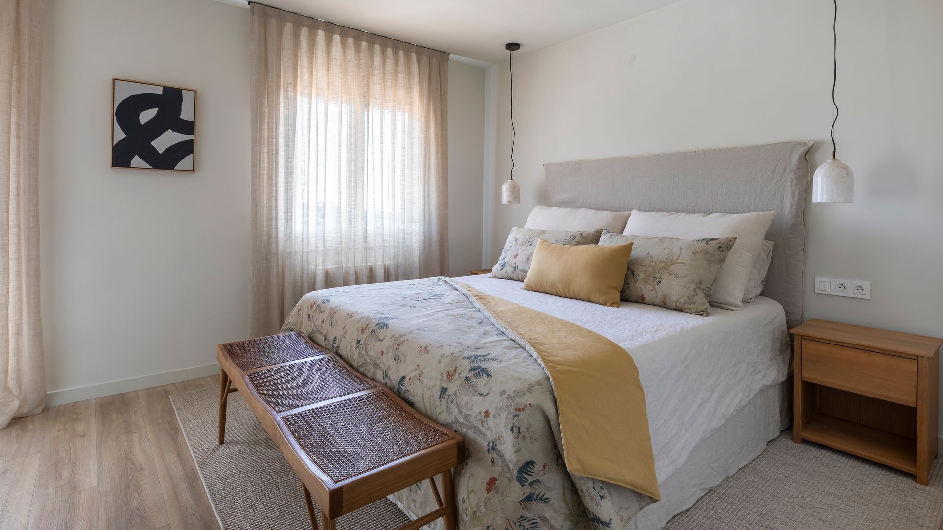 Dormitorio con cabecero alto tapizado, ventilador de techo, banco a los pies de la cama, alfombra, mesita de noche de madera, cortinas, lámparas de techo sa ambos lados de la cama