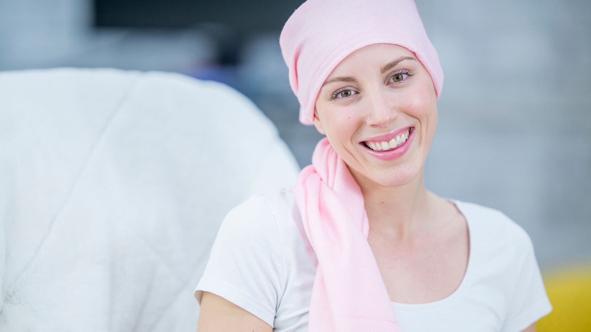 Paciente de cáncer de mama con pañuelo rosa sonriendo a cámara 