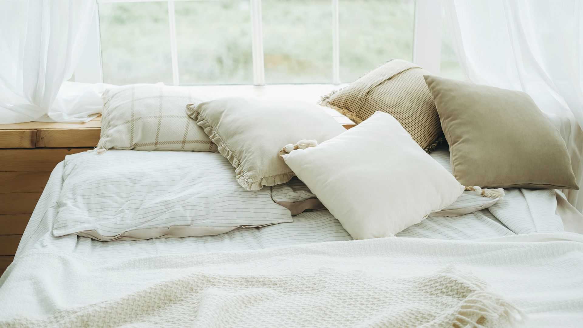 Cama con ropa textil en tonos beige, blancos y verdes. El cabecero es, en realidad, una ventana al jardín.