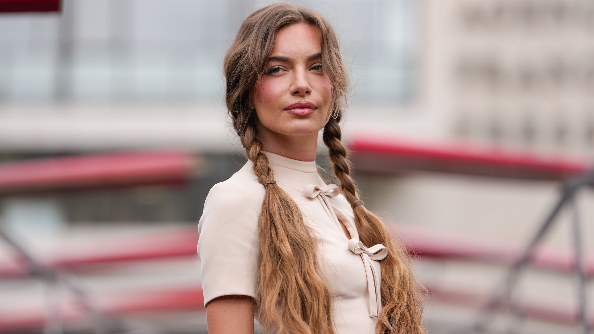 PARIS, FRANCE - JULY 07: A guest wears a cream-colored, short-sleeved top featuring a high collar and a keyhole cutout with a bow detail at the front. Hair is styled in two long braids, outside Georges Hobeika, during Paris Fashion Week - Haute Couture Fall/Winter 2025/2026, on July 07, 2025 in Paris, France 
