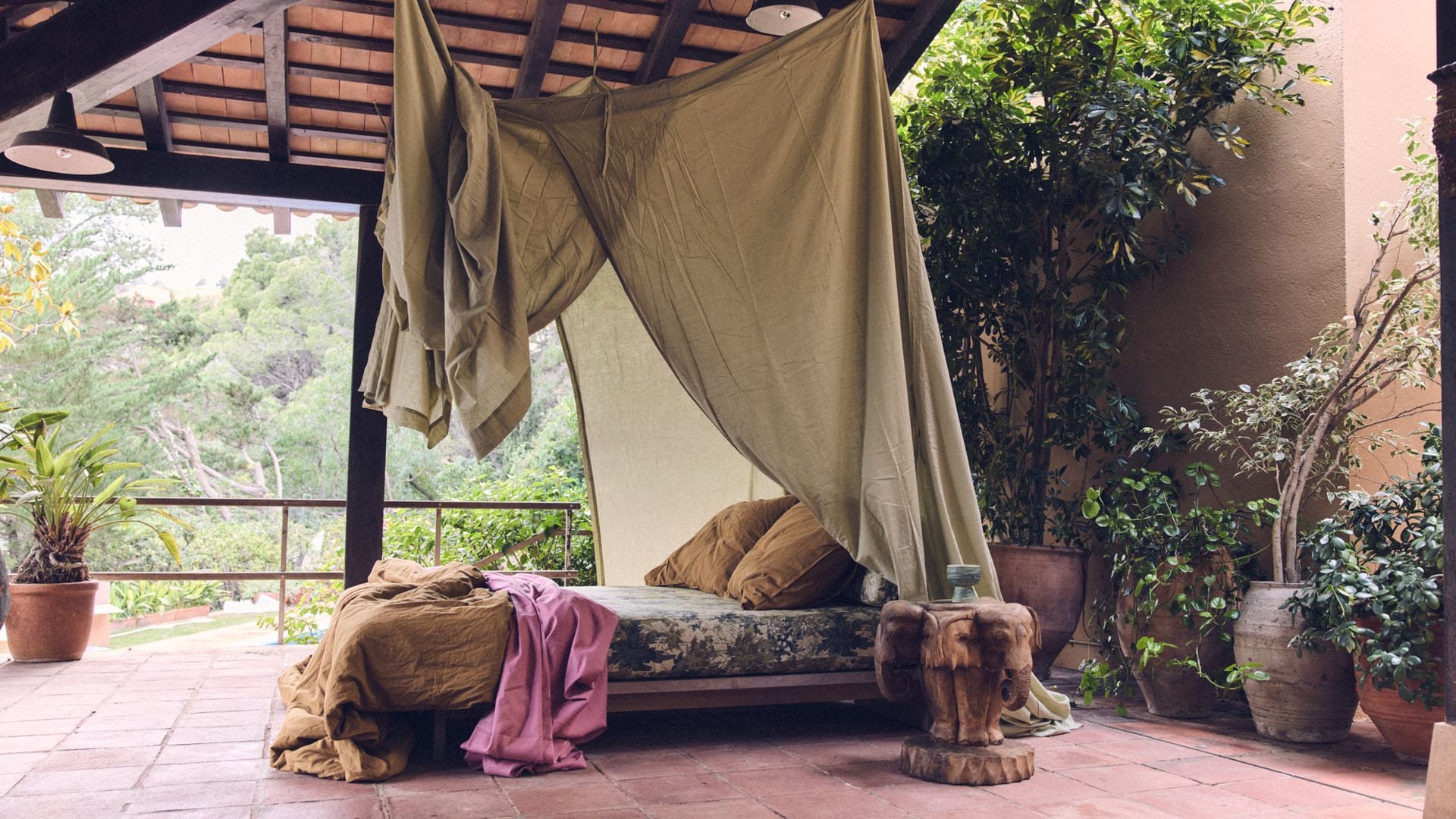 Dormitorio en la terraza con plantas, dosel, techo de madera con fibras vegetales, suelo de barro,