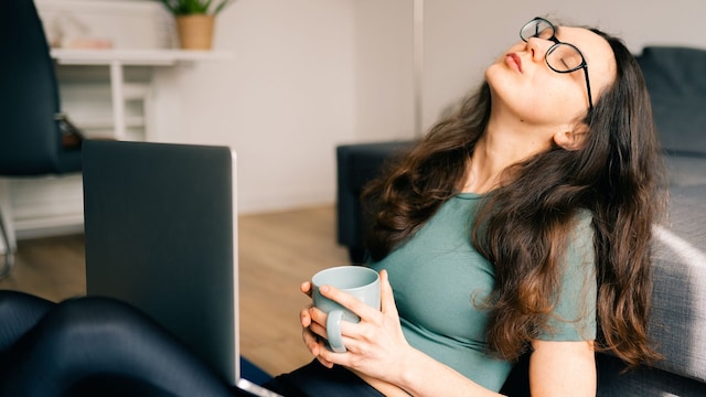 Mujer joven descansando en el suelo con el ordenador portátil y una taza de café en la mano