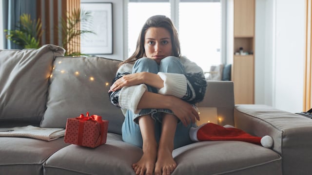 mujer triste y pensativa sentada en el sofá en Navidad