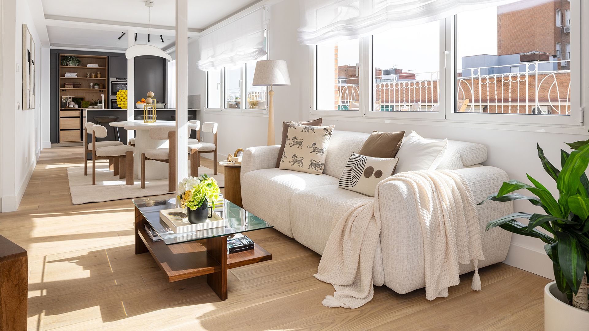 Salón comedor de color blanco, columnas en el centro, suelo de madera, sofá blanco, ventanas con estores blancos, mesa de centro 