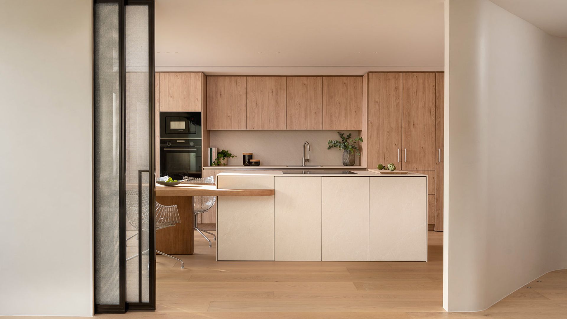 Cocina semiabierta con puertas correderas de cristal, cocina de madera con isla blanca, armarios superiores hasta el techo