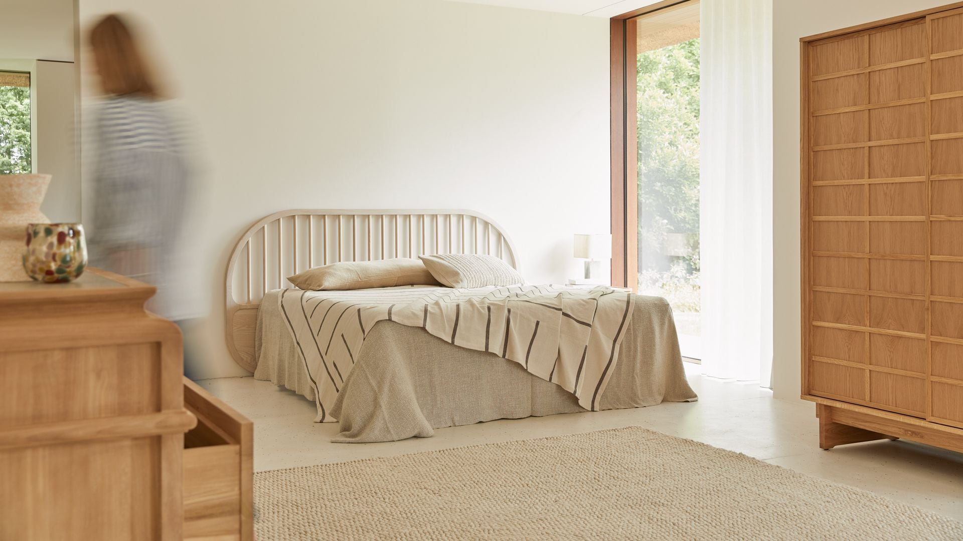 Dormitorio con cama de matrimonio, ventanal, armario, cabecero de lamas, alfombra, ropa de cama beige, plaid de rayas