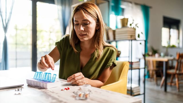 Mujer joven organizando la medicación en un pastillero semanal sentada en la mesa de su casa