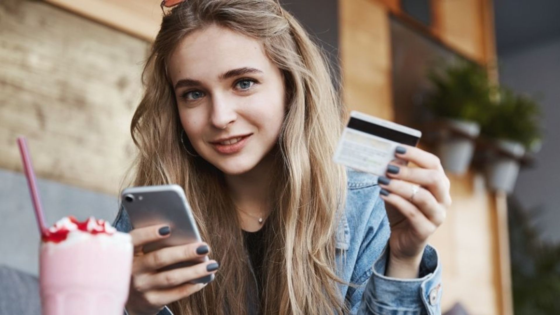 Adolescente con tarjeta de crédito y teléfono en la mano