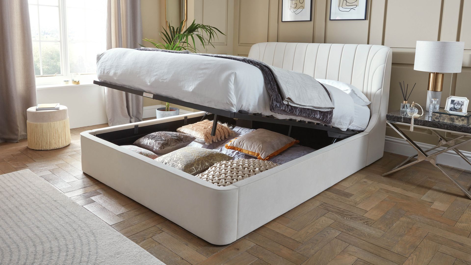 dormitorio con canapé abatible con cojines y ropa de cama, cama tapizada en color blanco, paredes con molduras en beige, ventanal con cortinas, alfombra, mesita de noche metálica