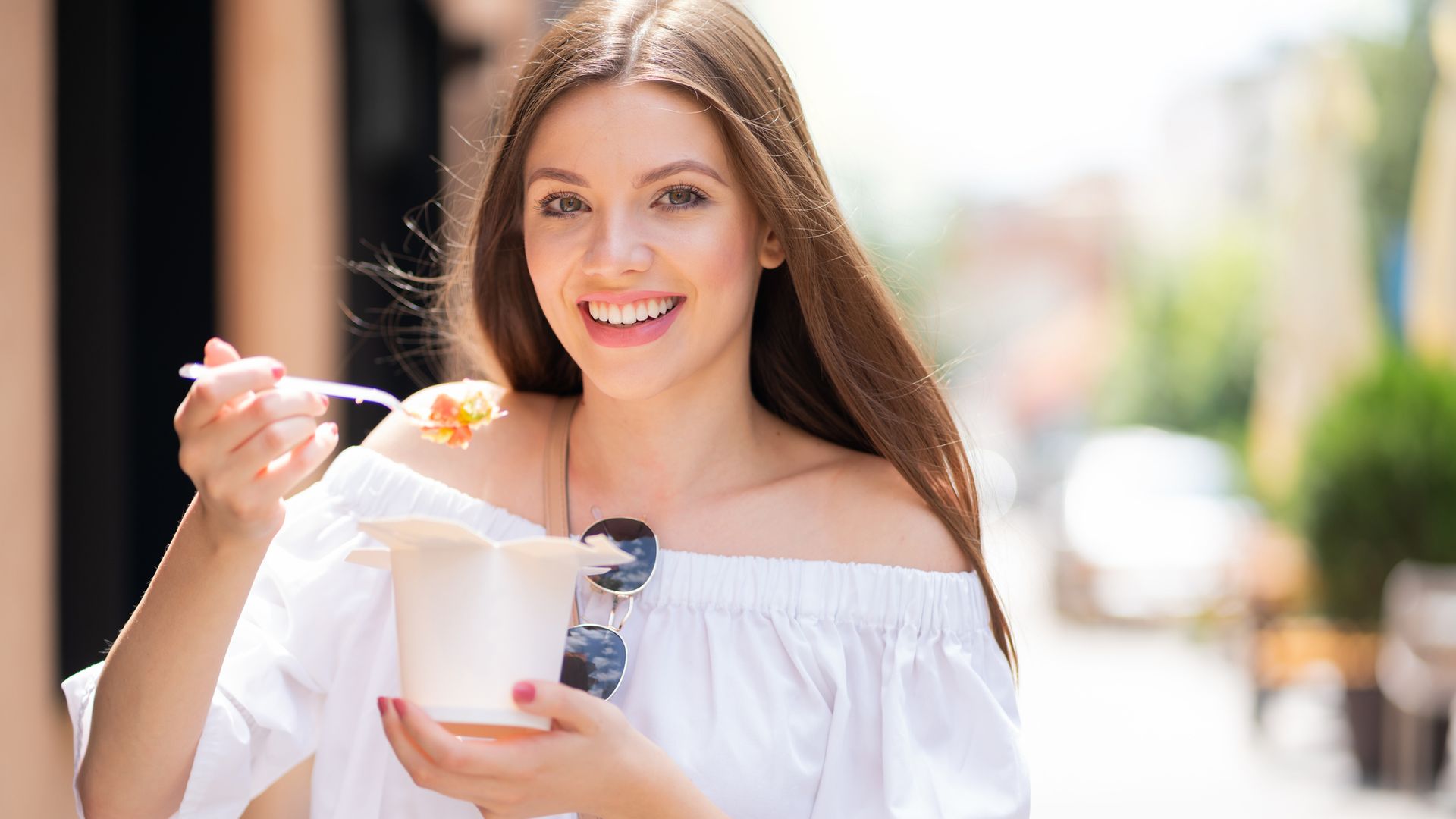 Mujer sonriendo comiendo pasta por la calle 