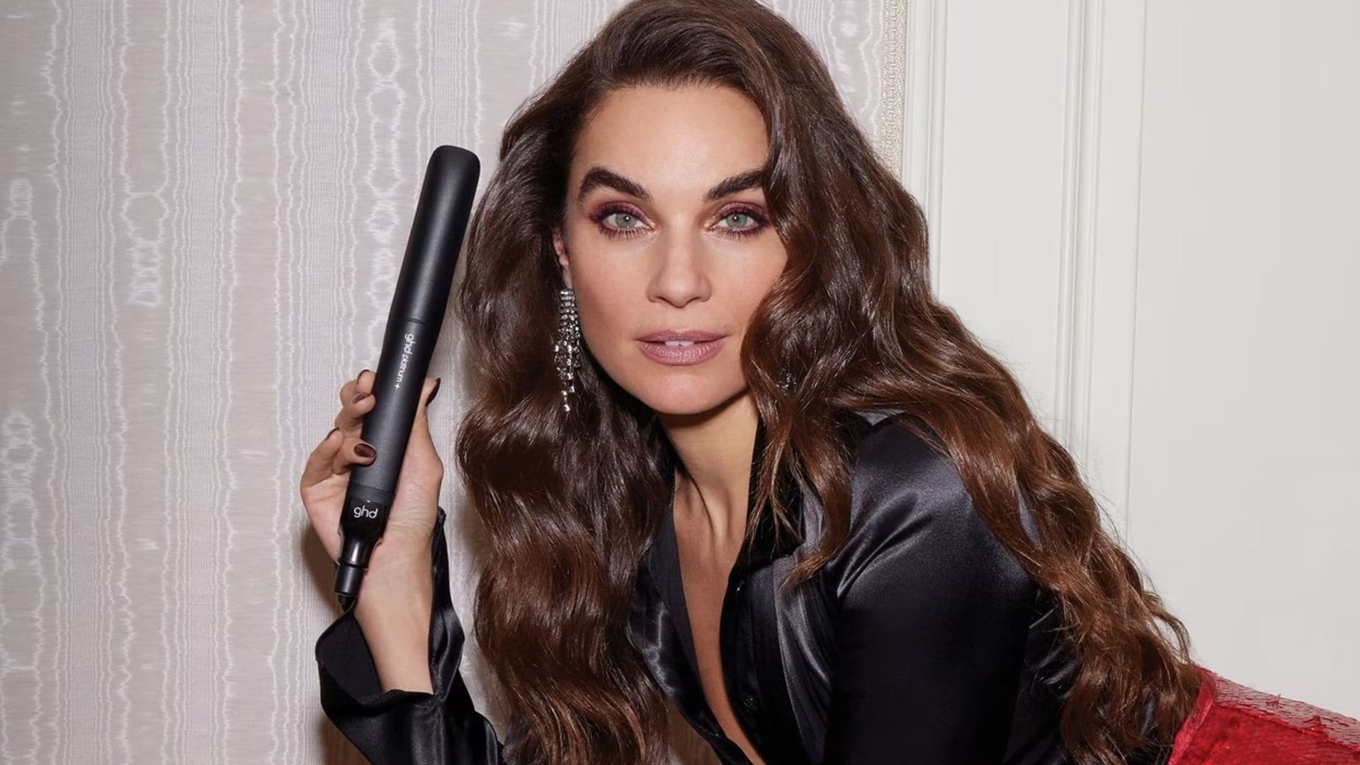 Mujer con pelo ondulado vestida de fiesta, con planchas de pelo y cepillo ghd en la mano