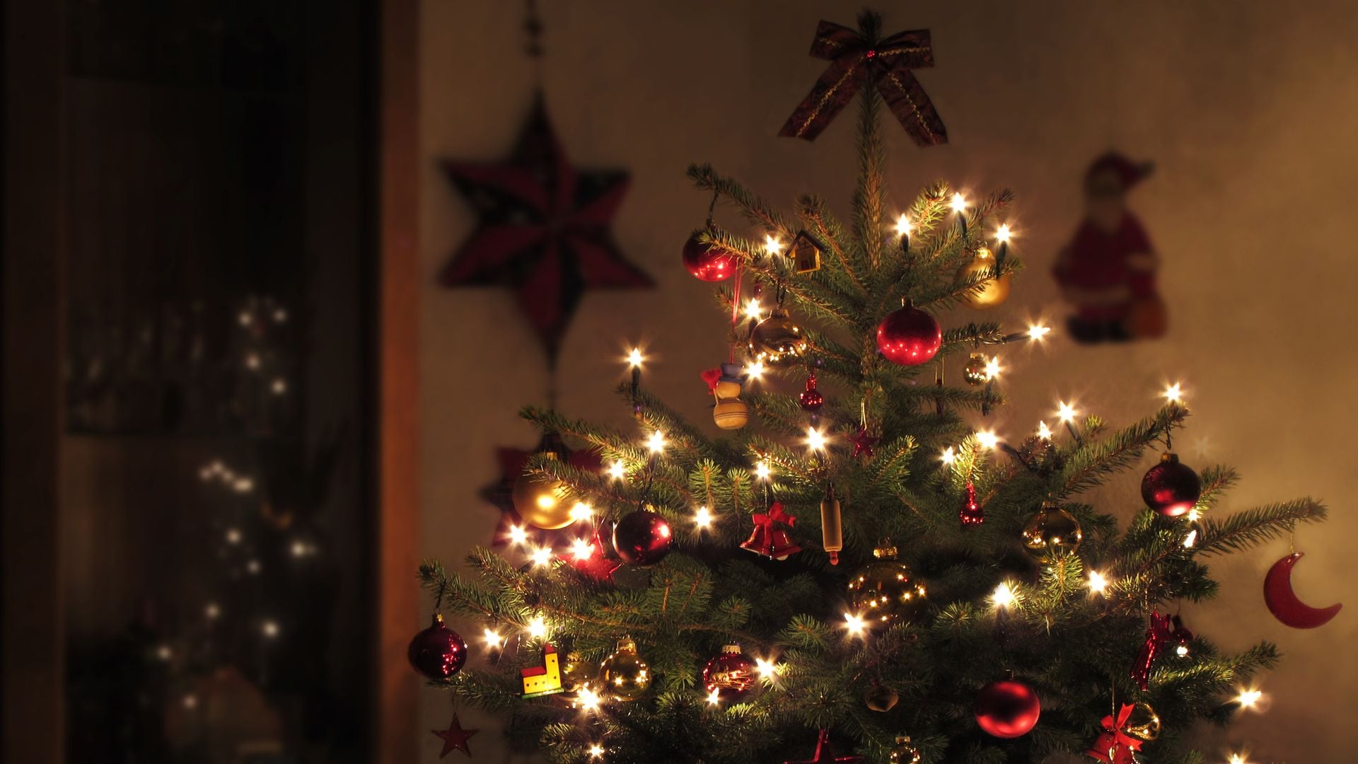 Árbol de Navidad cerca de una ventana, decorado con adornos rojos y una guirnalda de luces que se refleja en la ventana.