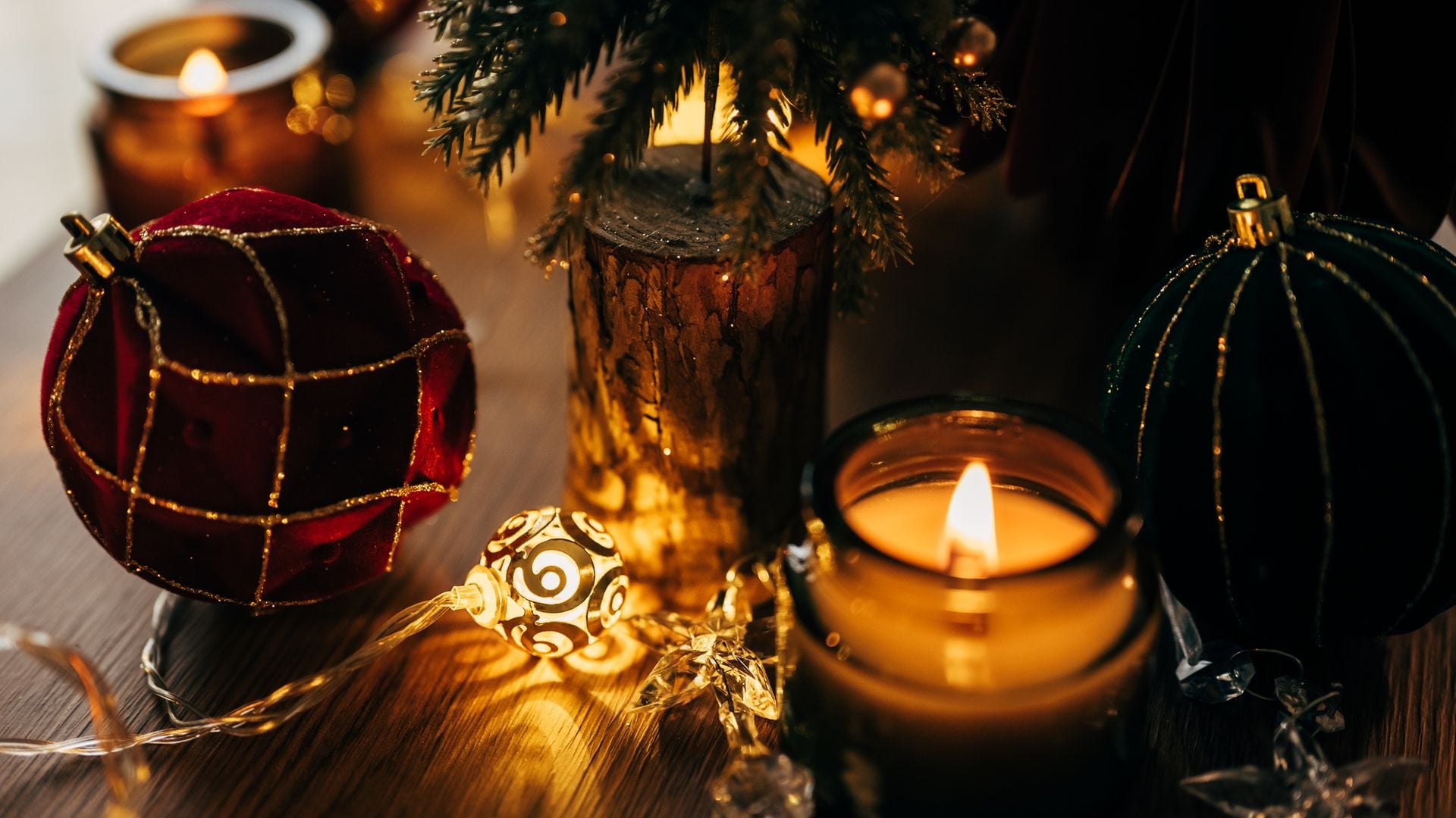Velas por Navidad con bolas en granate y verde encima de una mesa con árbol.