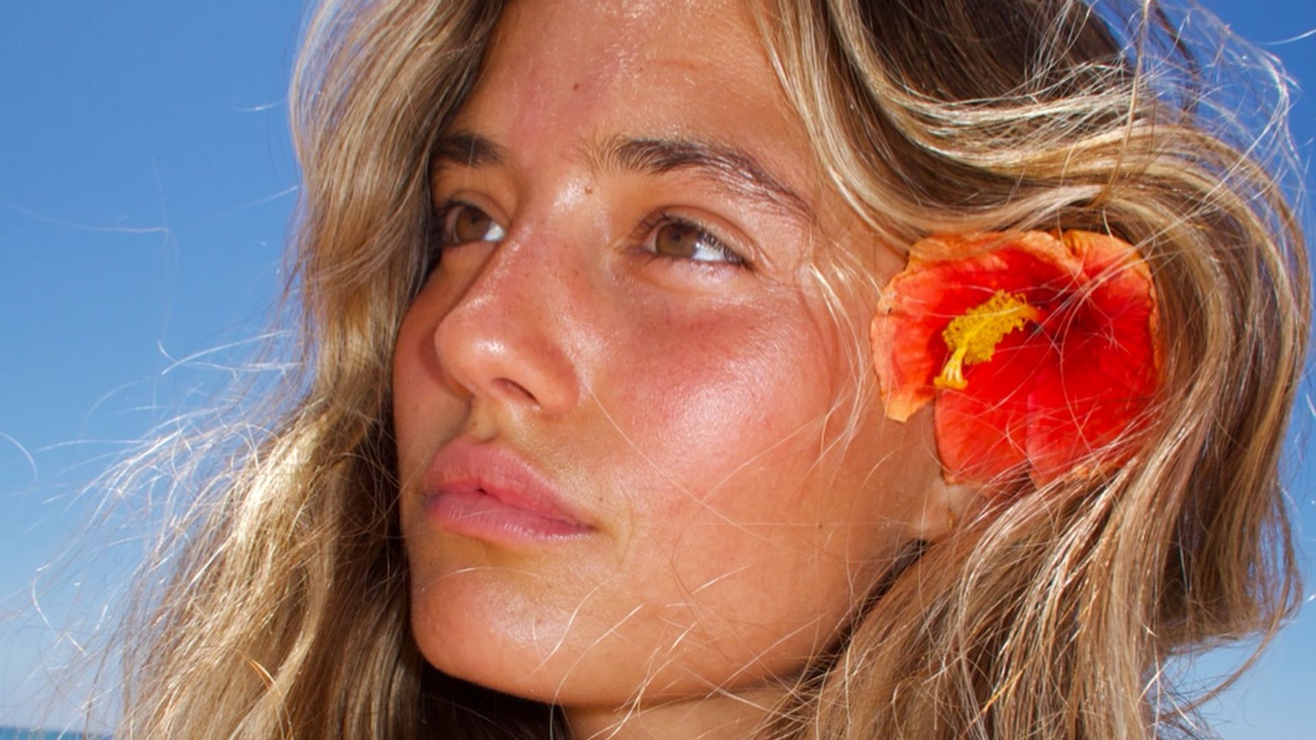 Chica con el pelo rubio dorado en la playa con flor roja