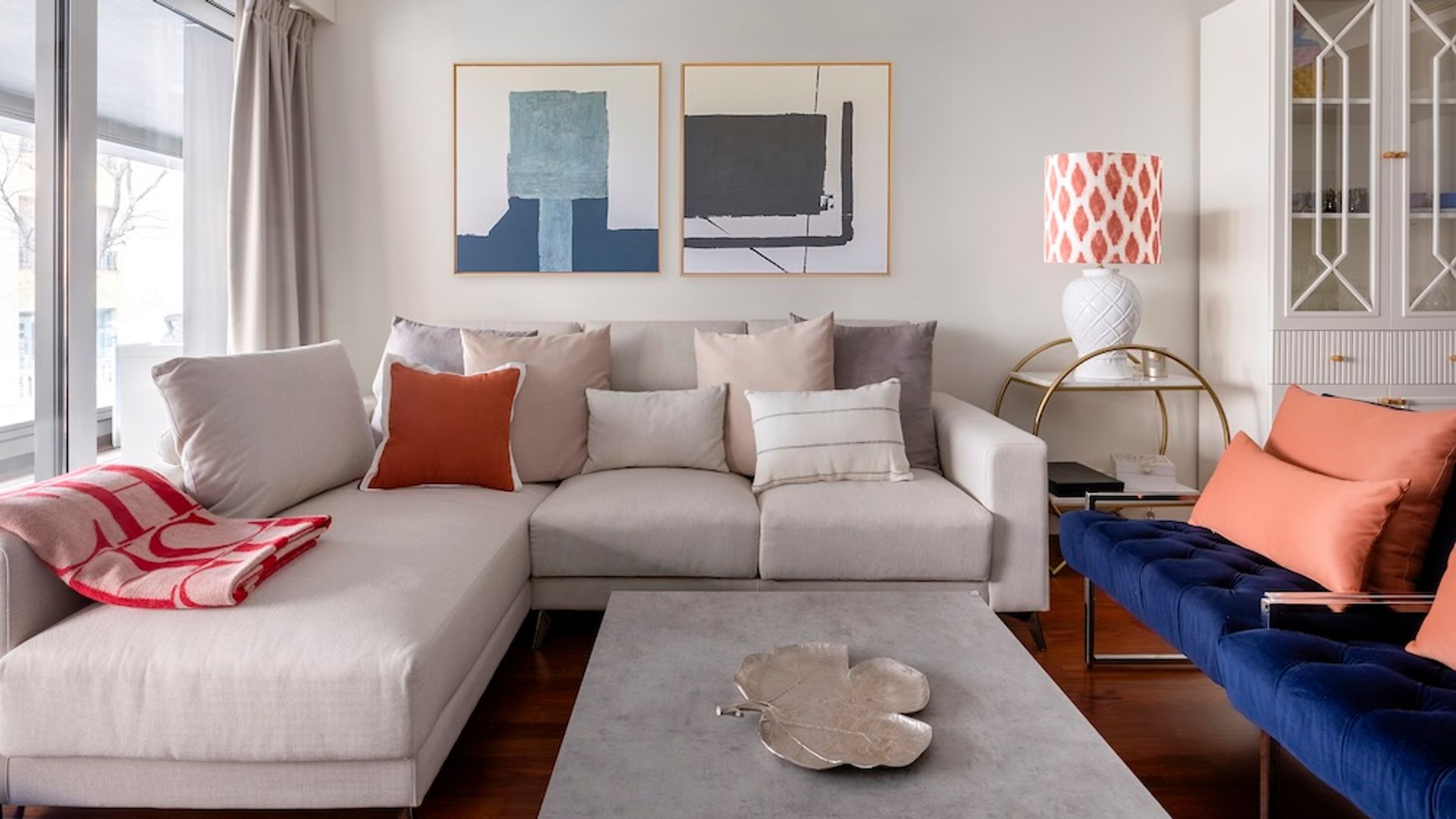 Salón con sofá blanco, cojines mantita sobre el sofá, cuadros en la pared del sofá, butacas azul eléctrico