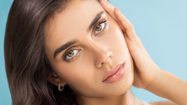 Rostro de mujer joven morena con ojos verdes y piel lisa y luminosa