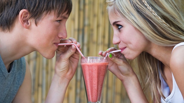 Adolescentes beben un batido del mismo vaso con pajitas