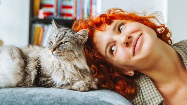 Mujer pelirroja en actitud cariñosa con su gato