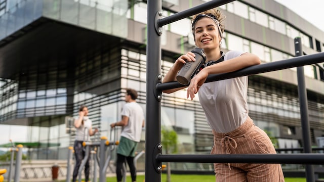 mujer joven sonriente haciendo un descanso tras un entrenamiento en la calle, bebiendo agua