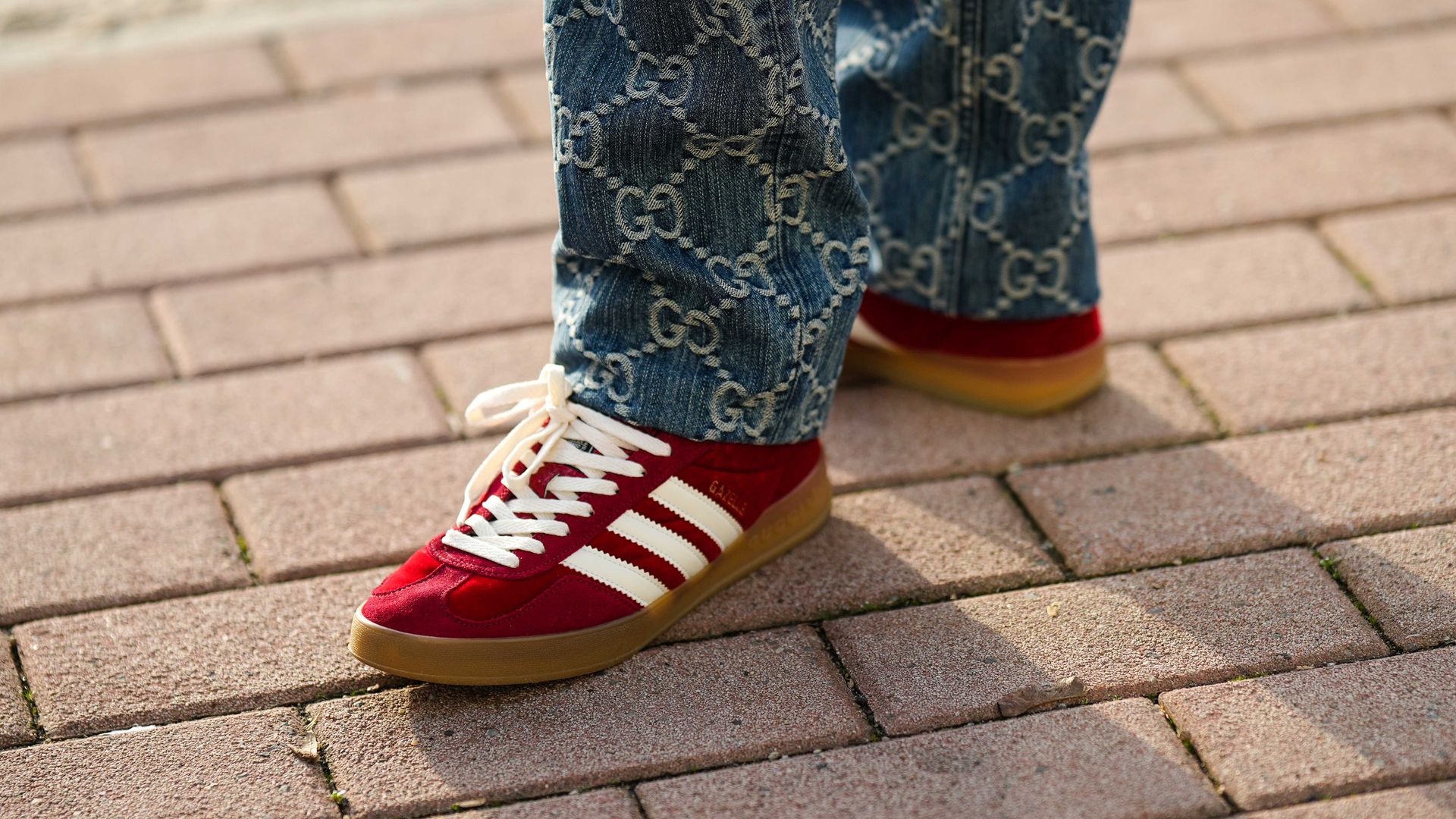Fotografía de los pies de una mujer en la calle con pantalones vaqueros de Gucci y zapatillas rojas Gazelle de Adidas