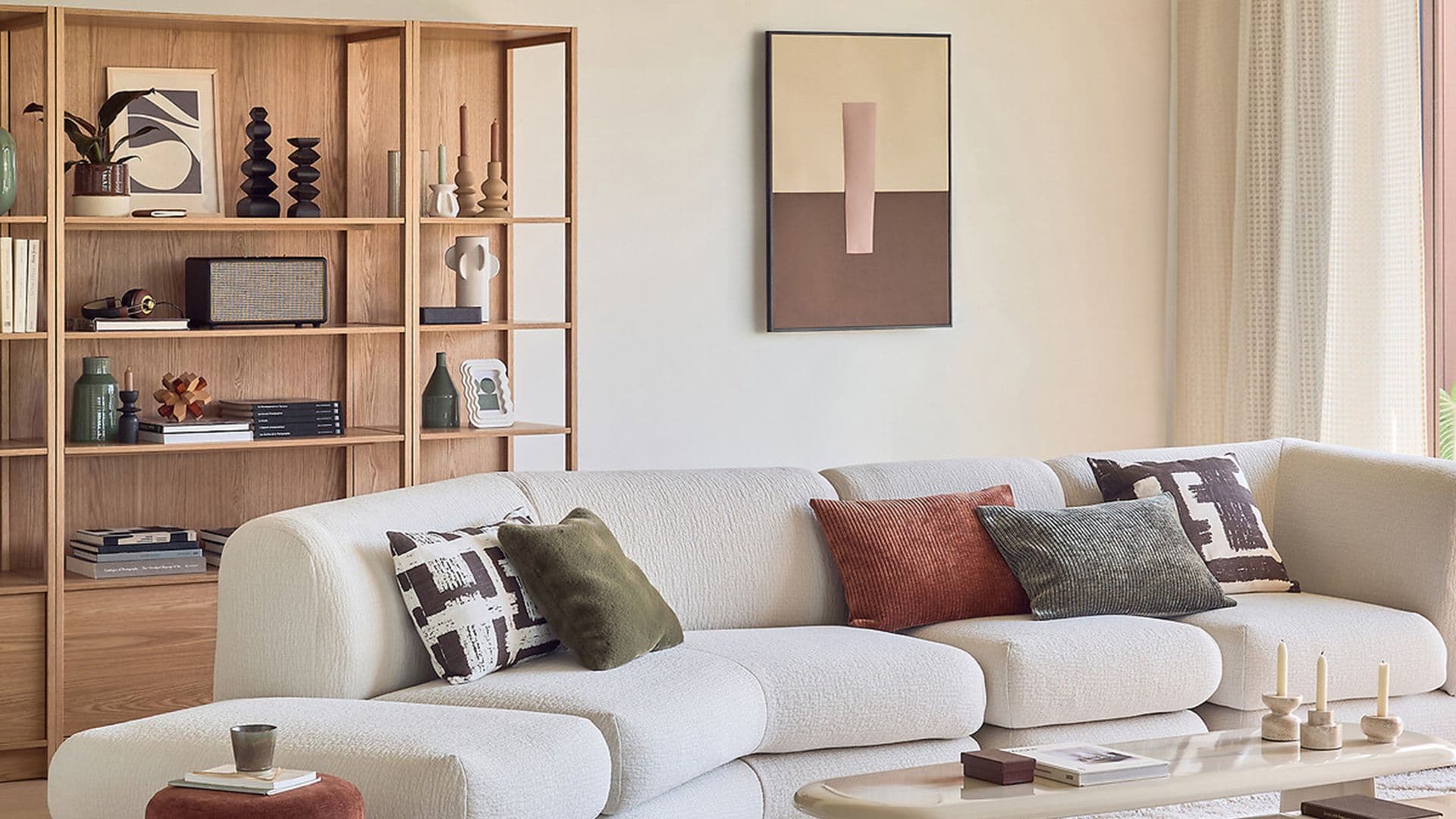 Salón con sofá blanco, alfombras de pelo, pufs, cojines de colores, estantería de madera, cuadro en la pared